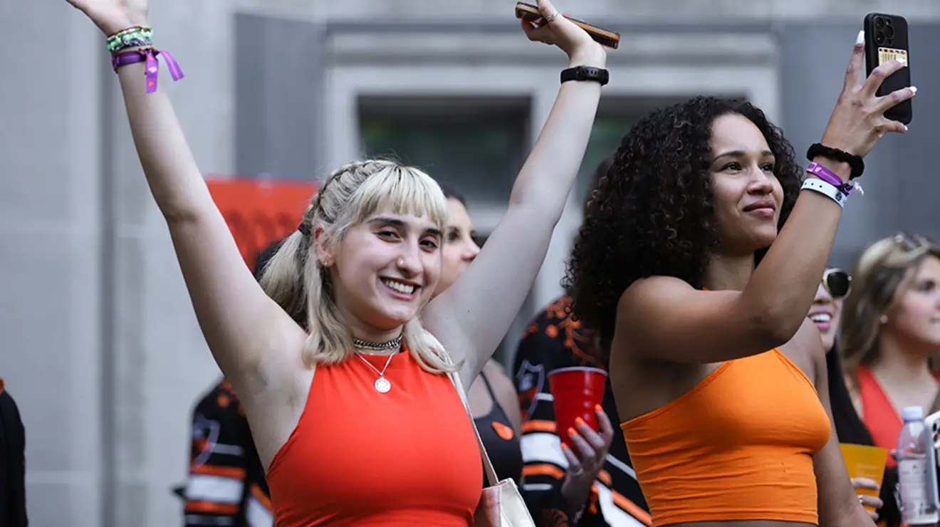 PRADE23_Allison-84.jpg A girl raises up her arms; another girl next to her takes a photo with her cell phone.