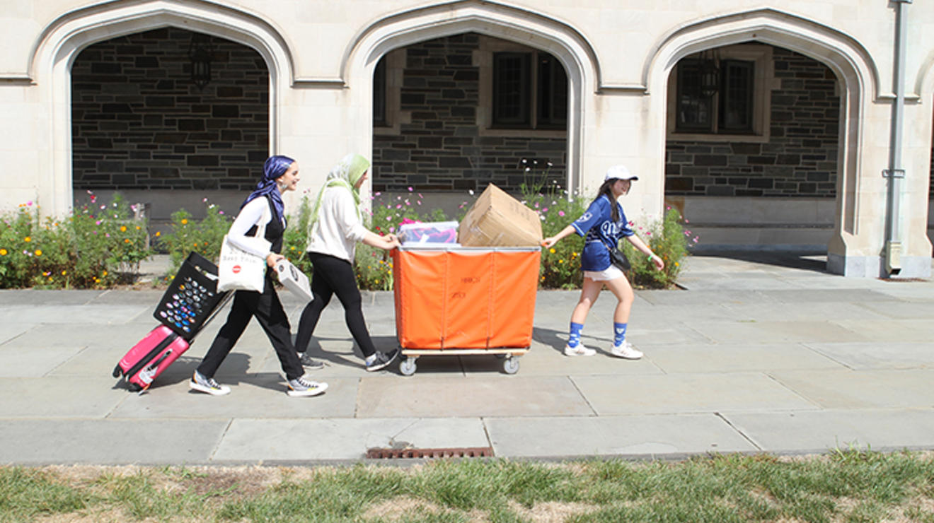 Three women push and pull a large orange bin.