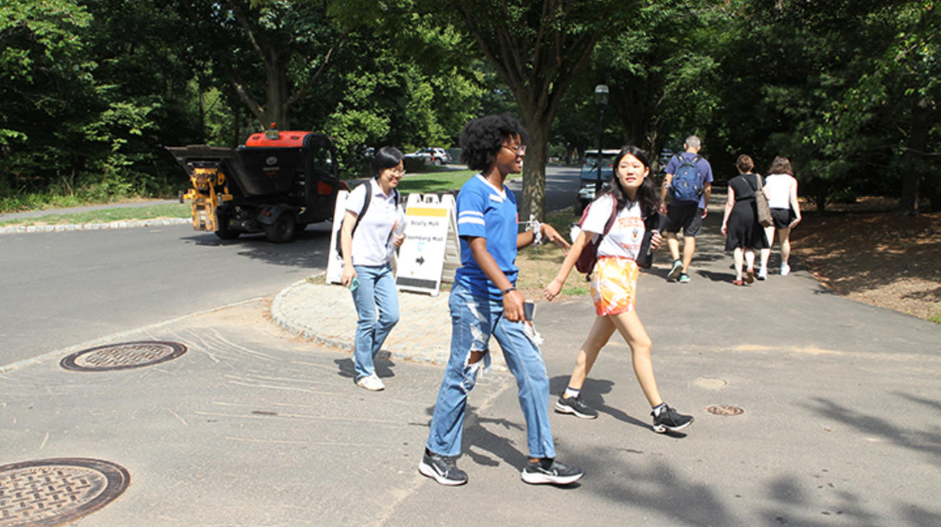 Students walk across a street with trees in the background.