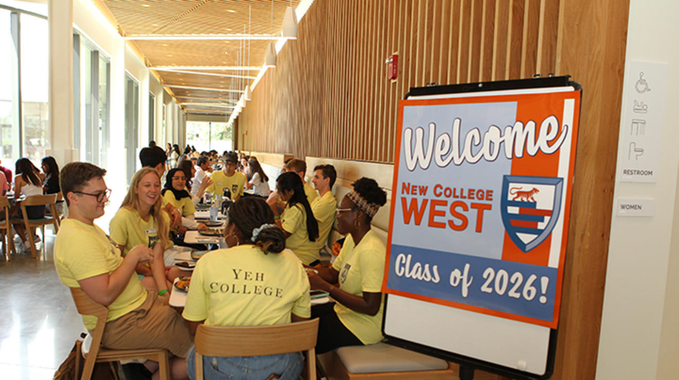 Students in yellow shirts sit around tables next to a sign reading, "Welcome Class of 2026! New College West."