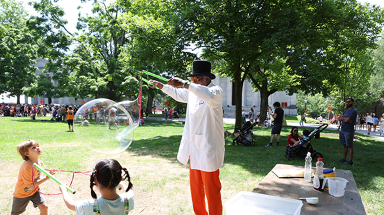 A man blows giant bubbles for two children with a rope-based bubble wand.