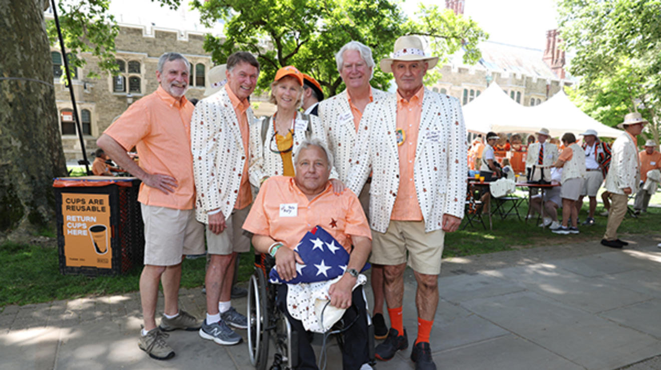 Five friends stand behind a man in a wheelchair holding a folded American flag.