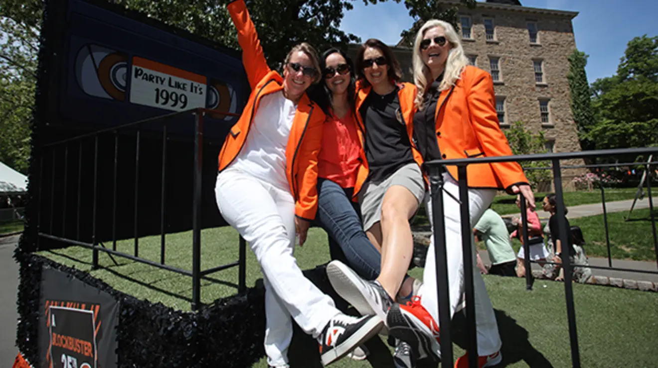 ReunionsSlideshow18.jpg Four friends pose next to a sign that looks like a videocassette and reads "Party like it's 1999."