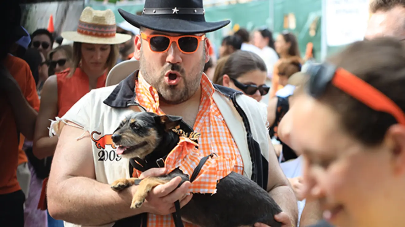 ReunionsSlideshow19.jpg A man in the P-rade wears orange sunglasses and a black cowboy hat and carries a dog.