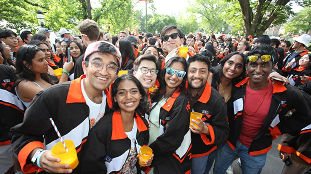 A group of young alumni hold drinks and pose for a photo at the P-rade.