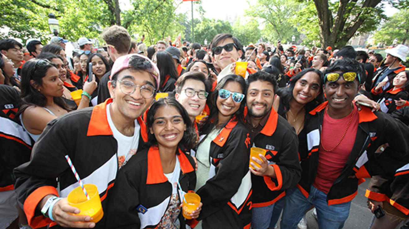 A group of young alumni hold drinks and pose for a photo at the P-rade.