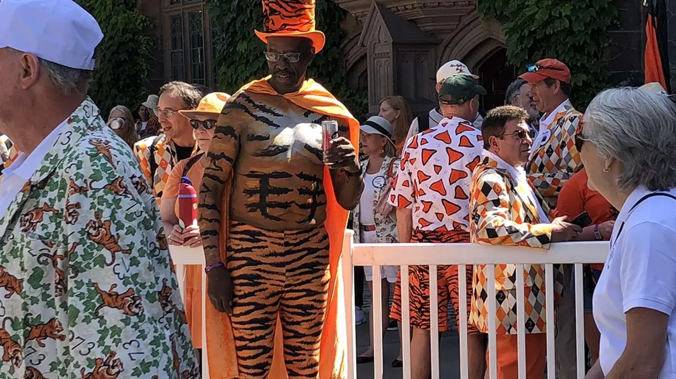 Tall man wearing a tiger striped hat and leggings, and an orange cape.