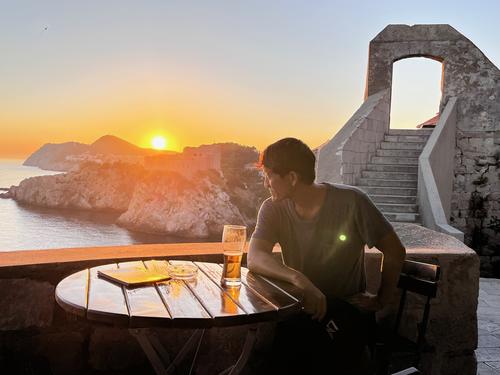 Darren Joe ’02 sits at a table at sunset over Fort Lovrjenac. A stone staircase is seen over his shoulder to the right.