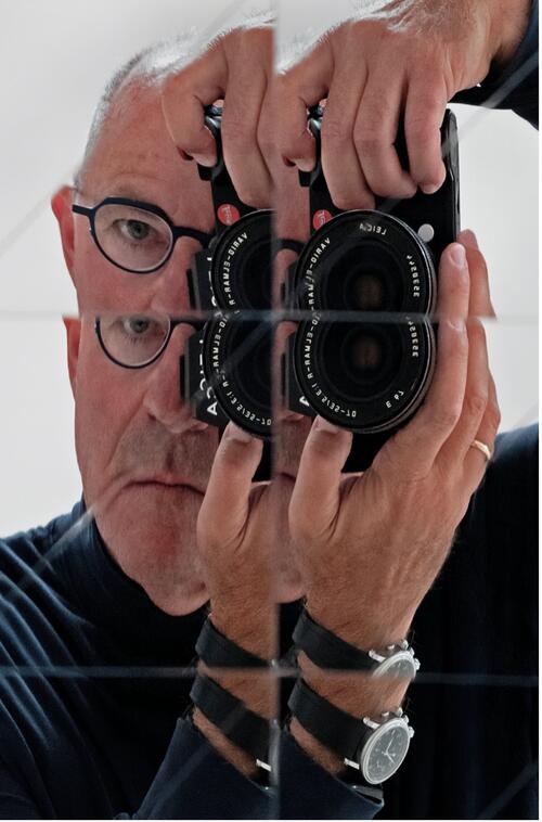 DanielSpitzer79.jpg A man aims a camera at a paned mirror that causes overlapping identical images.