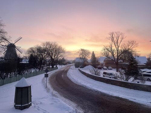 A pink and orange sunrise sky with snow covered buildings. 