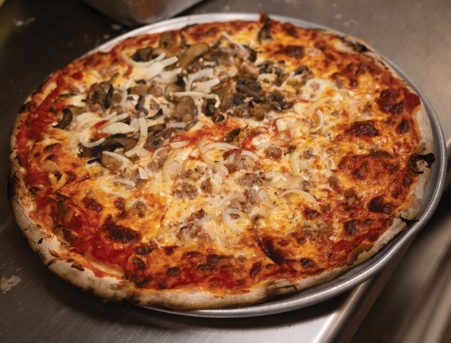 A close-up of a pizza with onions and sausage on half and onions and mushrooms on the other half.