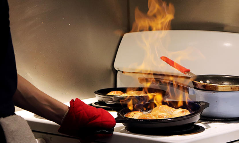 This is a photo of a student's hand wearing an oven mitt shaking a flaming skillet over a dorm-size stove.