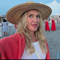Tiger-Travles_Newport-Rhode-Island_Jennifer-Roosth-headshot.jpg Photo of Jennifer Roosth in a straw sun hat and red sweater standing on the beach