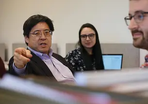 Professor Sam Wang points toward the camera; he's in a room where students sit at computers but look at him.