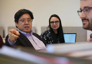 Professor Sam Wang points toward the camera; he's in a room where students sit at computers but look at him.