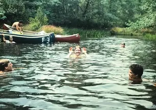 Students swimming in a river with canoes on the bank