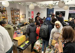 People pack into the Little Shop of Kindness; round paper lanterns and an ivy garland hang overhead.