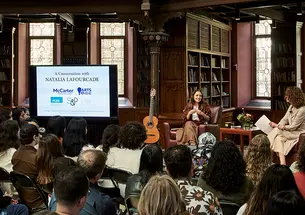 Two women and a guitar next to a screen, speaking to a crowd.