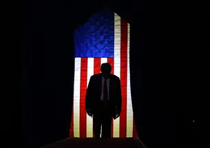TrumpInFrontofFlag.jpeg Trump standing in front of a lit U.S. flag surrounded by darkeness