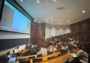 The USG meets in the Arthur Lewis Auditorium on Nov. 10. There is a document projected on the screen behind the USG Vice President. Members of the USG have their hands raised to vote.