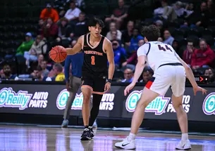 A basketball player wearing a Princeton jersey with a #1 on it, dribbles while facing off a defender.