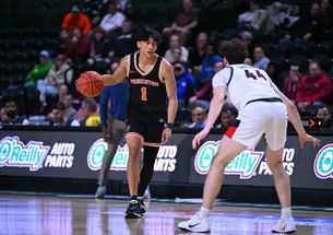 A basketball player wearing a Princeton jersey with a #1 on it, dribbles while facing off a defender.