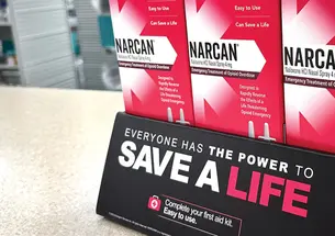 Pink boxes of Narcan tacked on counter with a sign that reads Save a Life