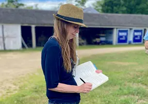 Michelle Lerner writes in a journal outdoors, a barn in the background.