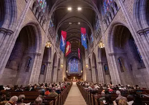 View down the aisle of the Gothic University Chapel, flanked by stone arches and full of people in the pews.