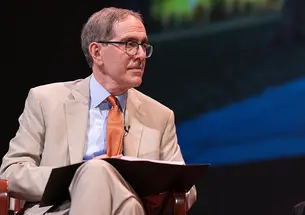 President Christopher Eisgruber ’83 sits on a stage wearing an orange tie and looks to his left.
