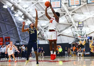 Princeton basketball player Dalen Davis '27, jumps while preparing to shoot a three. A player from Akron is jumping in front of him, attempting to block the shot. 