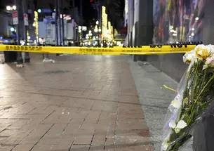 At night, a bouquet of flowers leans up against a building next to a brick sidewalk blocked off with caution tape.