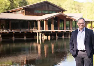 Jason Posnock ’94 stands in front of a pond and a rustic-looking building at the Brevard Music Center.