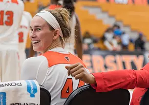 A Princeton basketball player smiles as she looks behind her from the bench on the side of a game.