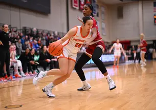 A Princeton basketball player dribbles inside, guarded tightly by a Harvard player. 