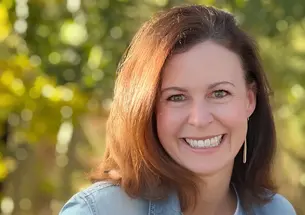 Andi Almond smiling for a photo with greenery in the background.