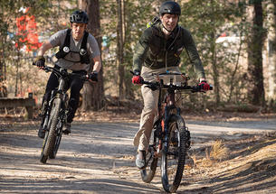 Two men ride bicycles.