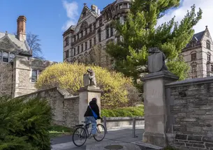 Bicyclist rides through a gateway flanked by two tiger statues holding shields