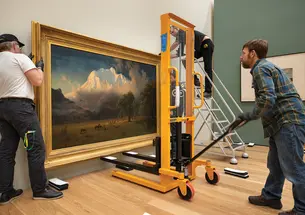 Two men move a large painting of a landscape into the new art museum. 