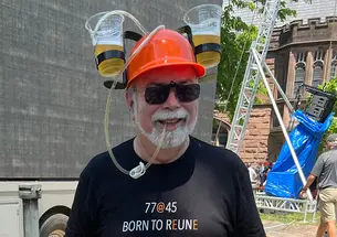 A man wears a hard hat with two cups of beer attached. His shirt reads "Born to Reune."
