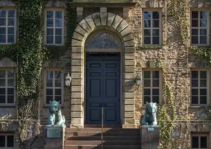 The front door to a stone building with paned windows, a stone archway over the door, and bronze tiger statues one each side.
