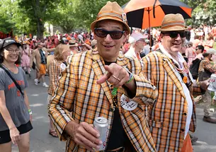 A man in an orange plaid blazer points to the camera during the P-rade.
