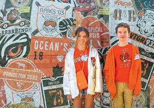 Violet and Everett Dutton standing in front of a collage of Class logos at Reunions 2023