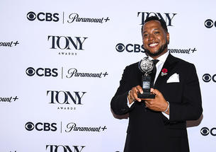 Branden Jacobs-Jenkins ’06 holds his Tony award in front of a step-and-repeat covered with logos for CBS, Paramount+, and the Tony Awards.