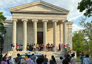 The front of Clio Hall, a classical-Greek-style columned building, with protesters standing on the steps. 
