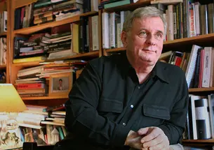 Edmund White in front of a bookcase jammed with books.
