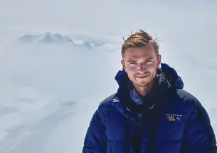 Ben Weissenbach in a blue puffer jacket on top of a snow covered mountain
