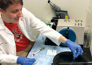 Graham Read ’15  wearing a white lab coat works in his lab