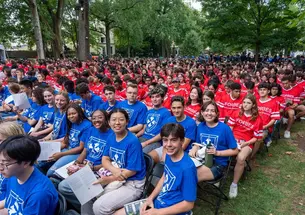 Students in blue and red residential college T-shirts seated outside Nassau Hall