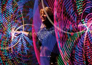 A woman spins colorful illuminated hula hoops around her wrists and ankles simultaneously. 